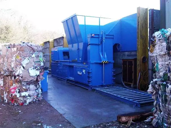Large blue machine outside with bales of compacted plastic surrounding it.
