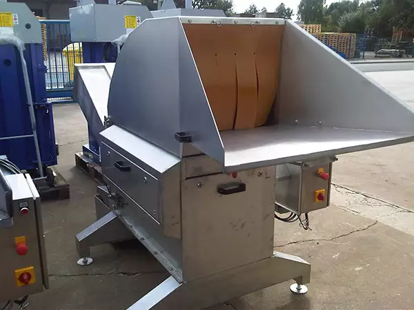 Angled front profile of the silver LiquiDrainer Bin Tipper Feed stood outside. A brown curtain covers the opening.
