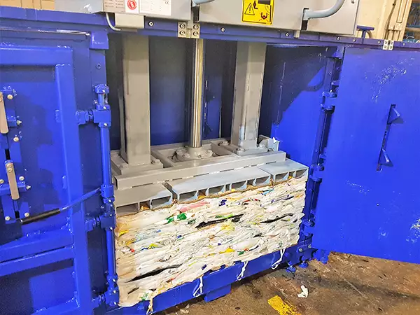 The doors of the MK1100 baler are open wide and inside can be seen compacted waste pushed down by the mechanism within.