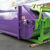 Angled side view of the purple and green RPK compactor standing outside The opening for waste disposal is closed.