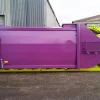 Side view of the purple and green RPK compactor standing outside. The bulk of the body is coloured purple and is bordered by a bright green frame.