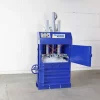 The blue BP10 stands against a white wall with its top panel ajar. Within, the compacting press can be seen pushing down on a mass of plastic waste.