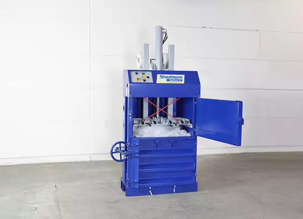 The blue BP10 stands against a white wall with its top panel ajar. Within, the compacting press can be seen pushing down on a mass of plastic waste.