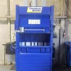 The BP53 compactor in blue stood on the concrete floor of a building. An opening at the front reveals the inside where trash is compacted.